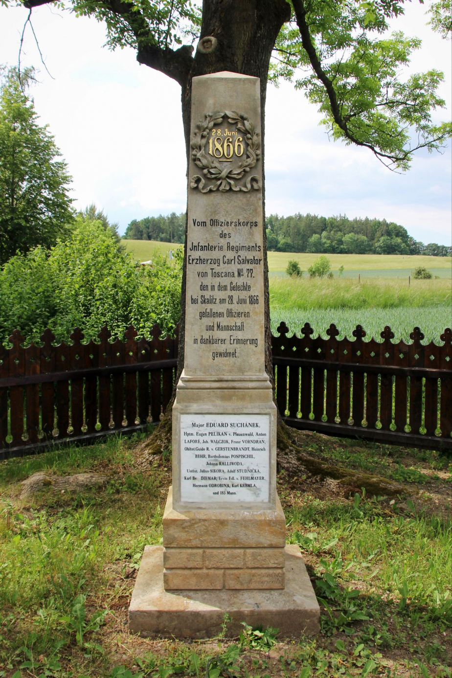 Pohled na zrestaurovaný pomník na vojenském hřbitově v České Skalici. V pozadí je vidět opravený plaňkový plot. 